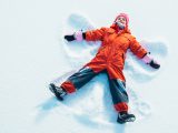 Little Girl wearing winter overalls makes a Snow Angel over fresh powder snow.